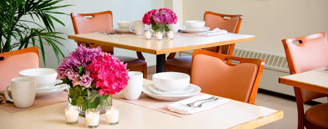 A neatly set restaurant table with bright pink flowers and elegant place settings.