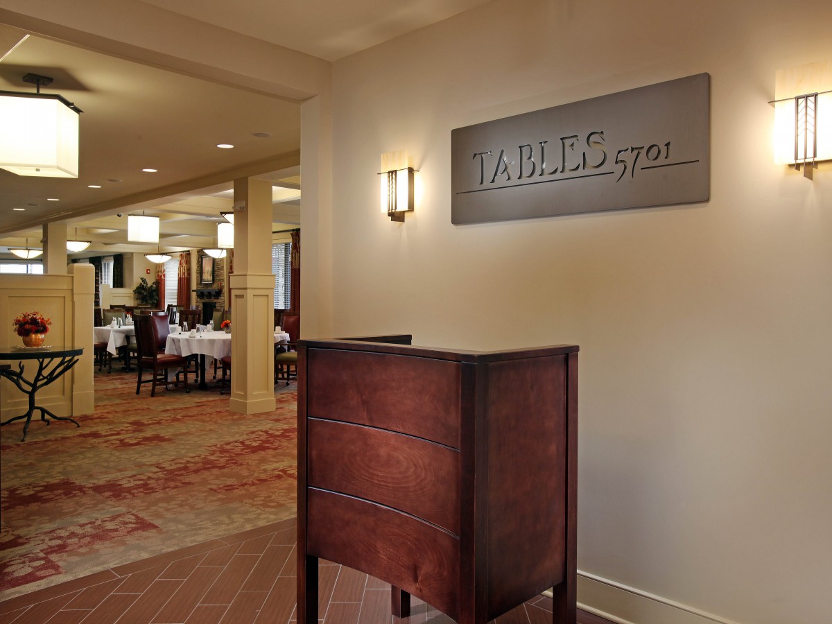 Entrance to a restaurant lobby with a wooden reception desk and visible dining area in the background.