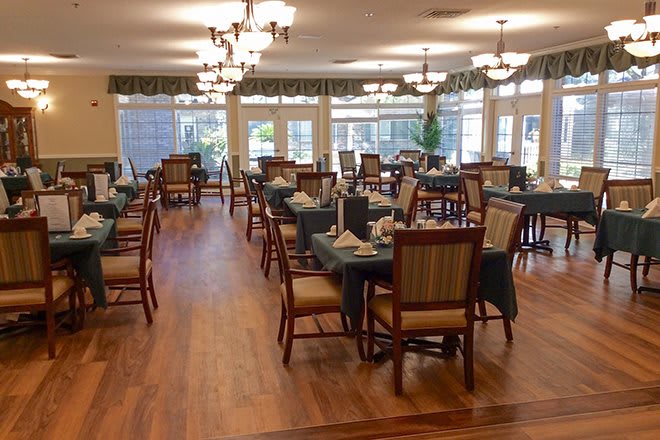 An elegantly set dining room with several tables and chairs, featuring chandeliers and a wooden floor.