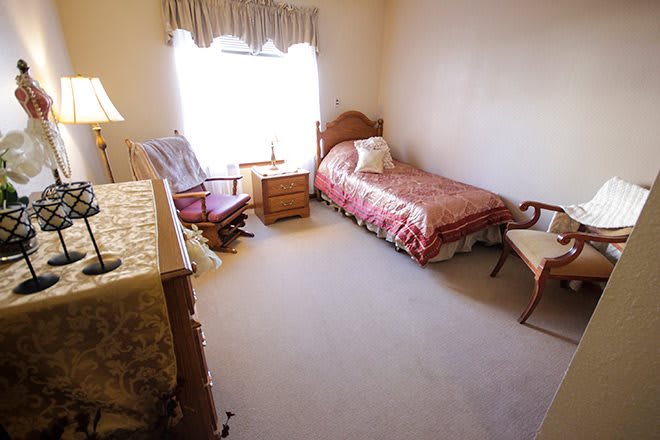 A cozy bedroom with a single bed, chair, and a window letting in natural light.