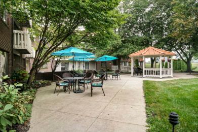 A serene outdoor patio area with tables, chairs, umbrellas, and a gazebo surrounded by lush greenery.