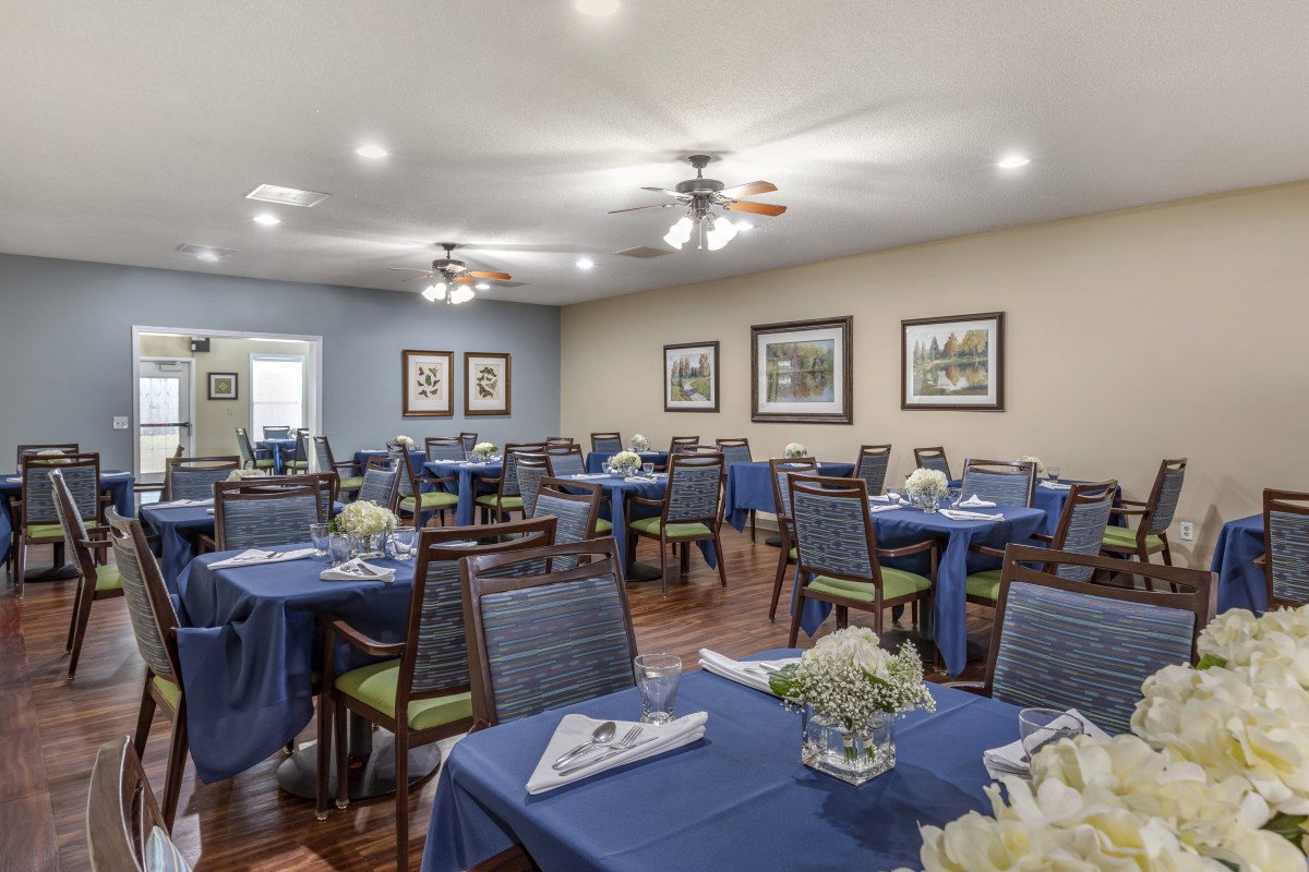 A well-arranged dining room with tables covered in blue tablecloths, surrounded by chairs and decorated with wall art.