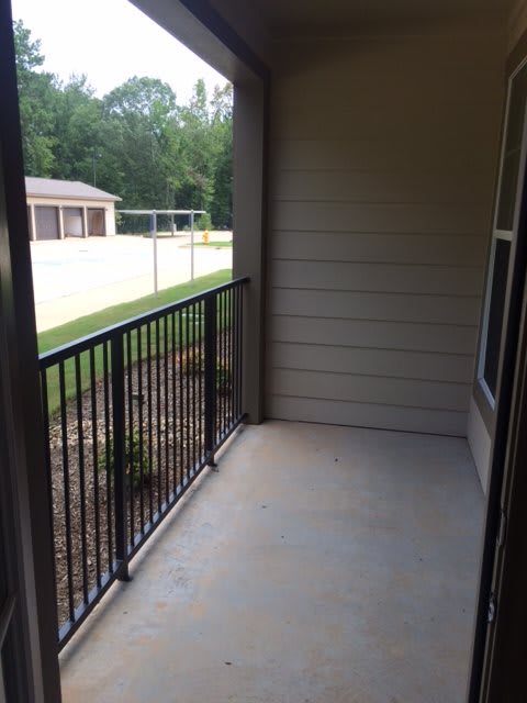 A small outdoor apartment balcony with a metal railing and view of a yard.