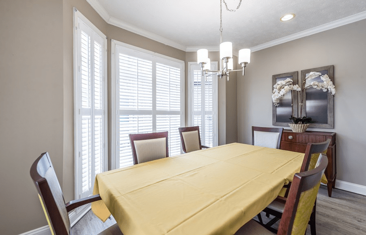 A well-lit dining room with a table covered in a yellow tablecloth and surrounded by chairs.