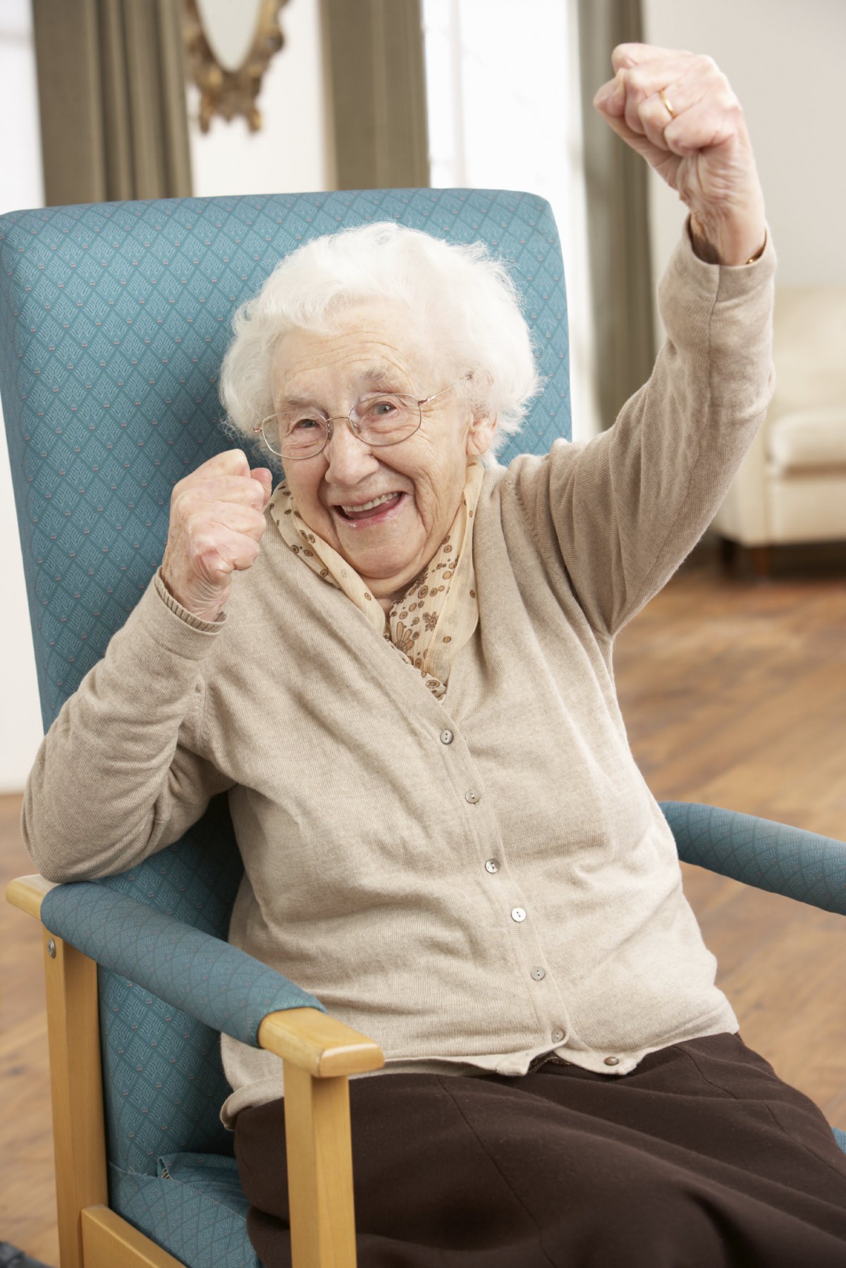 A joyful elderly woman celebrating while seated in a chair indoors.