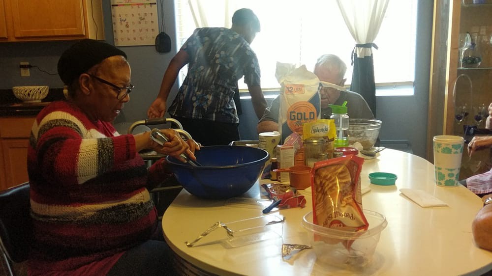 A group of people gathered around a table preparing food in a kitchen setting.