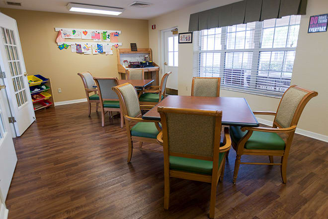 A cozy dining room featuring wooden tables and chairs, with natural light streaming through large windows.