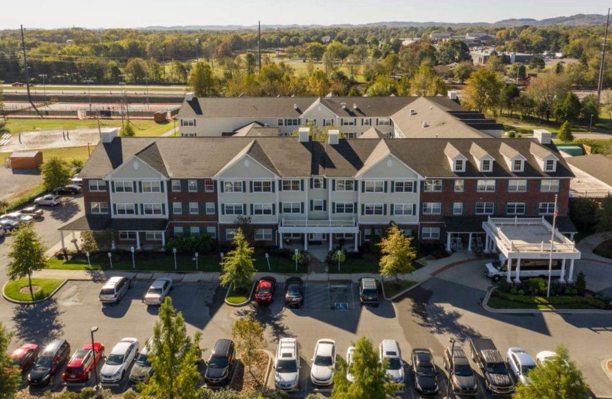 Aerial view of a suburban residential building with a parking lot surrounded by trees.