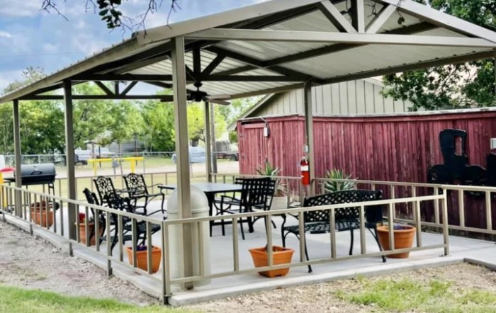 An inviting outdoor patio with a shaded seating area, complete with chairs, tables, and potted plants.