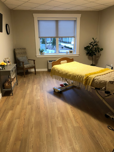 A serene healthcare room featuring a hospital bed with a yellow blanket, a comfortable chair, and natural light from the window.