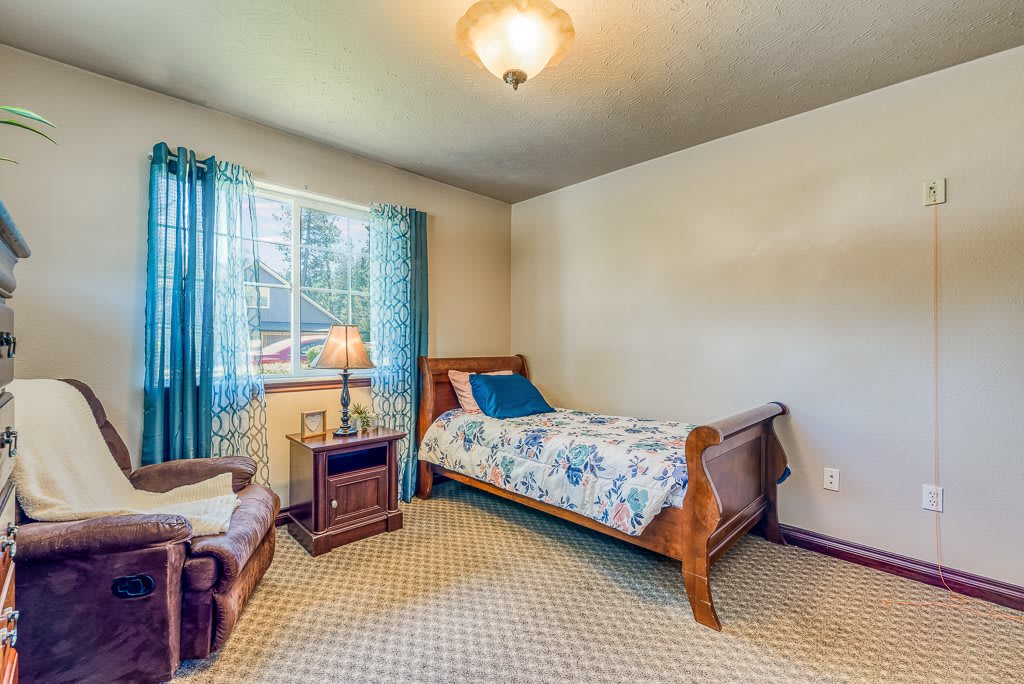 A cozy bedroom featuring a single wooden bed, carpeted floor, and a lamp on the nightstand by the window.