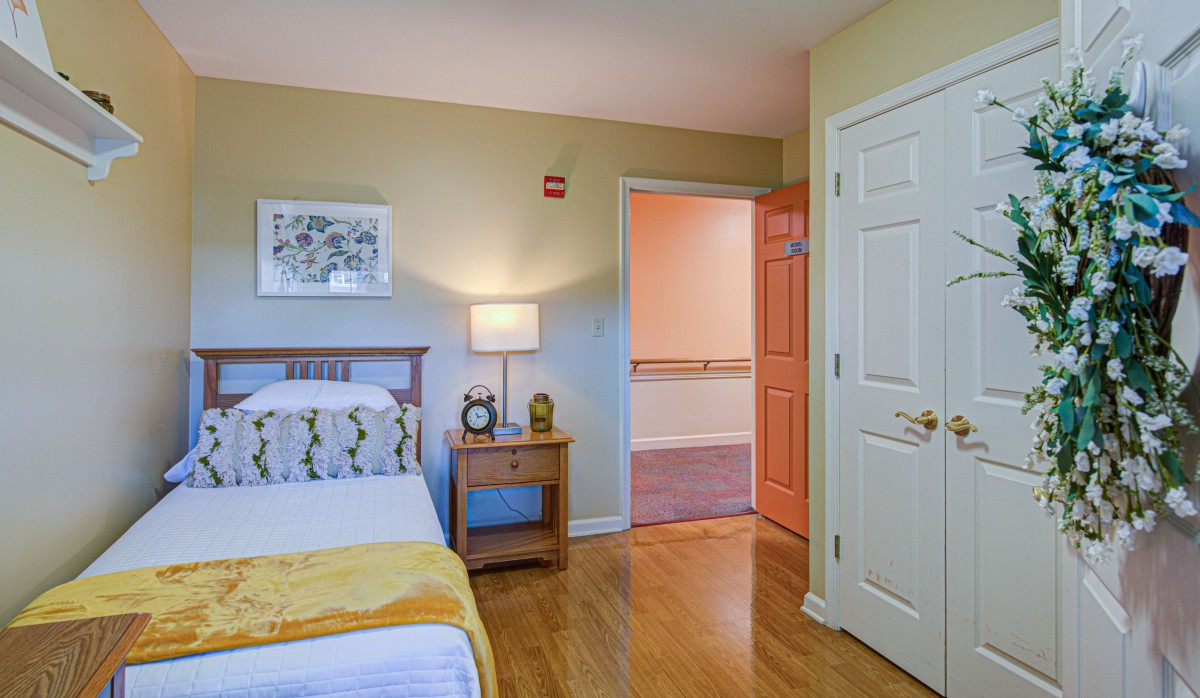 A cozy bedroom with a bed, nightstand, and lamp near an open door.