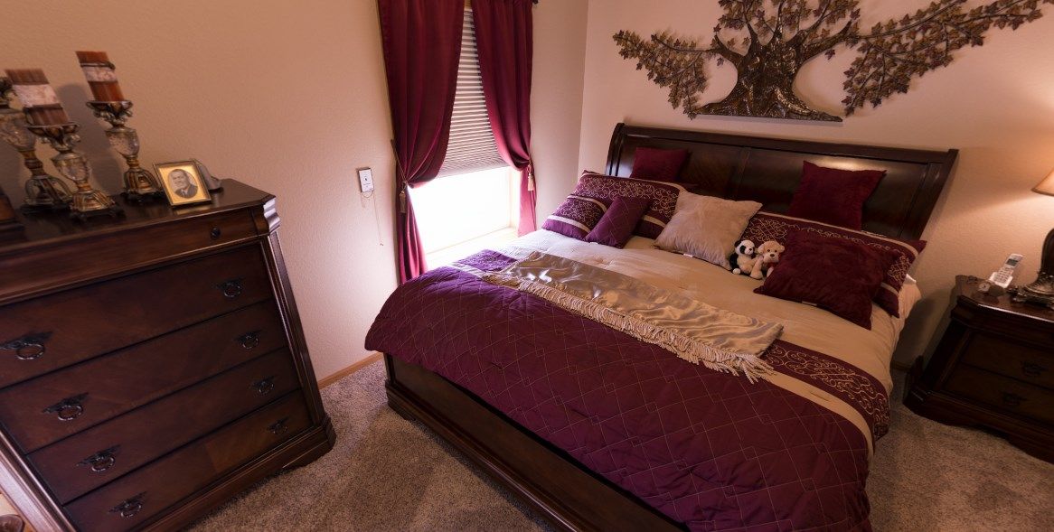 A cozy bedroom with dark wood furniture, purple bedding, and decorative pillows.