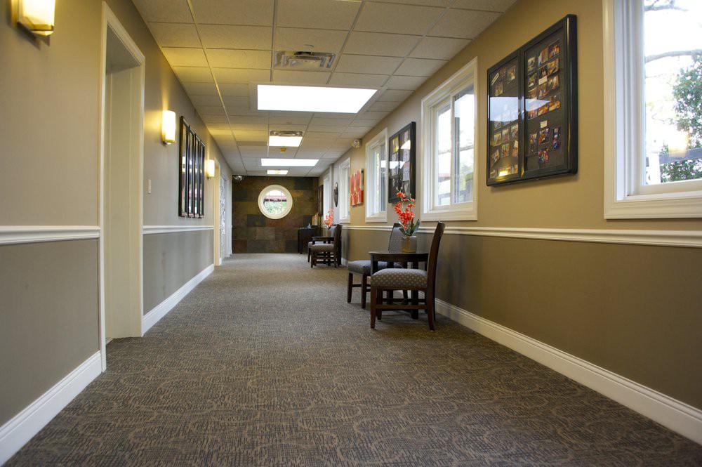 A well-lit hallway with chairs, artwork on the walls, and large windows.