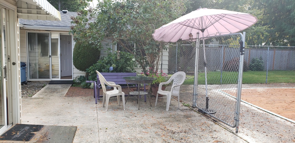 A cozy backyard patio with chairs, a table, and a pink umbrella.