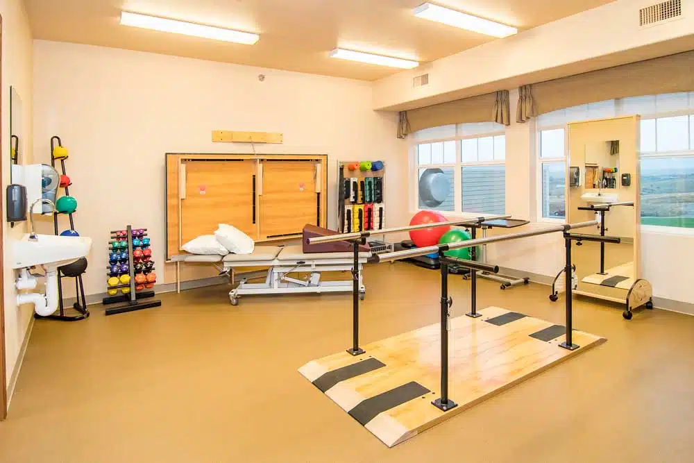 A well-equipped physical therapy room with parallel bars and various exercise tools.