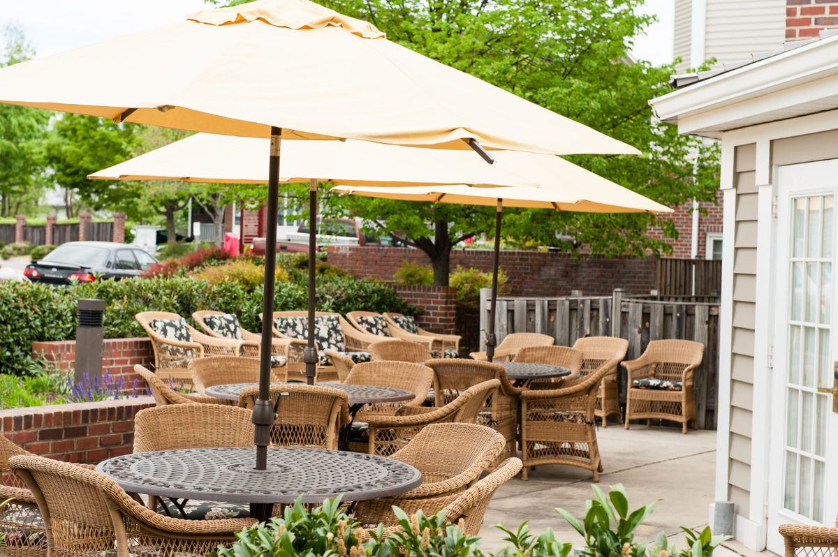 A peaceful outdoor patio area with wicker chairs and tables under large umbrellas, surrounded by greenery.