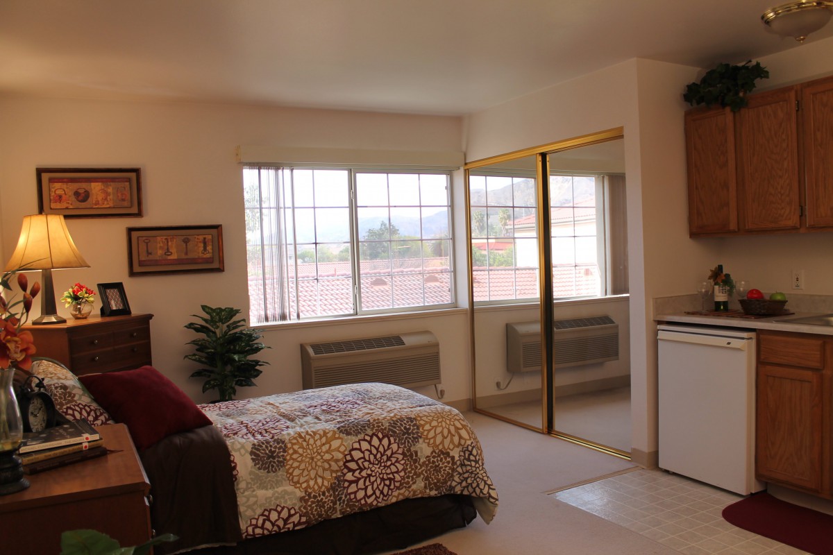 A cozy bedroom interior with a bed, large windows, and mirrored closet doors.