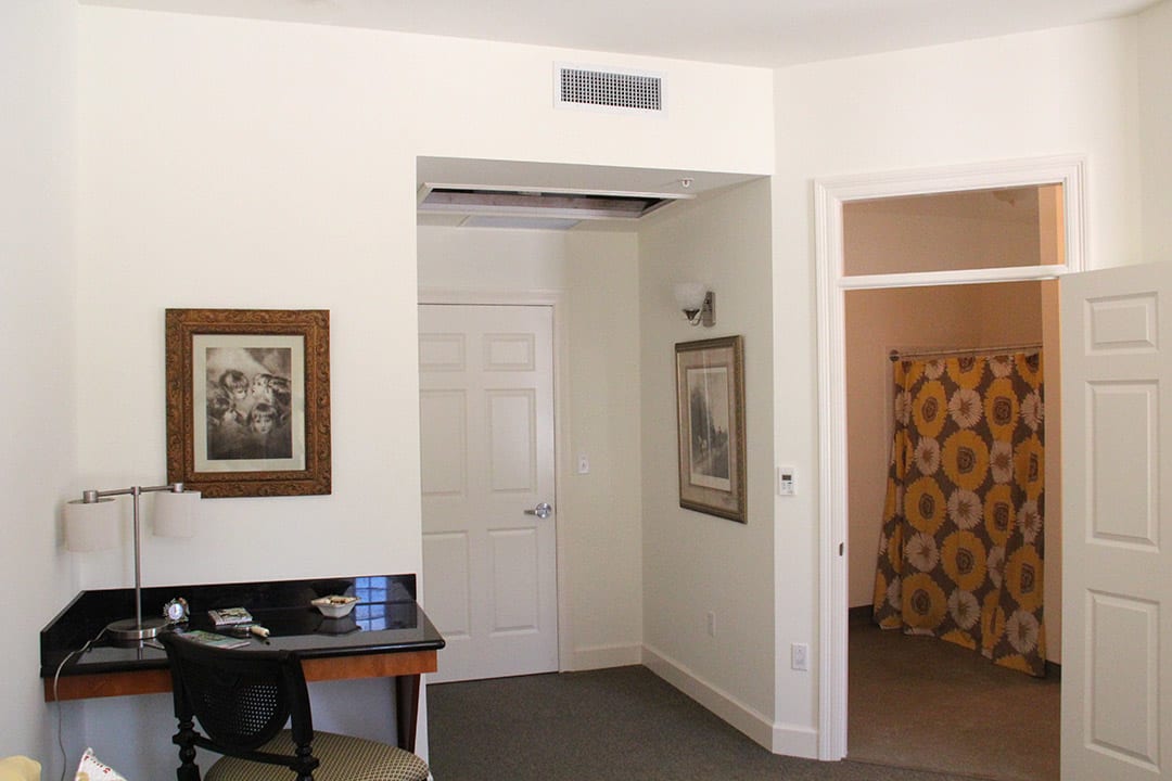 A hotel room interior with a desk, wall artwork, and open doorways.