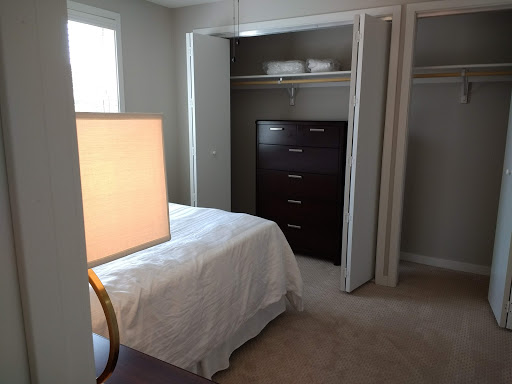 A cozy bedroom featuring a neatly made bed, a stylish lamp, and ample storage space with a dresser and closet.