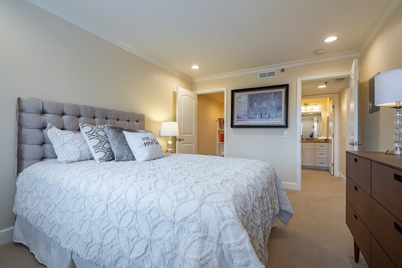 A modern bedroom with a neatly made bed, decorative pillows, and warm lighting.