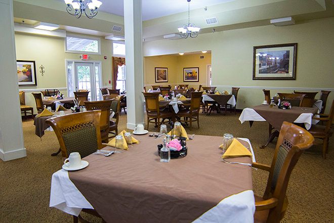A well-lit dining room with neatly arranged tables and chairs, each table adorned with table settings and folded napkins.