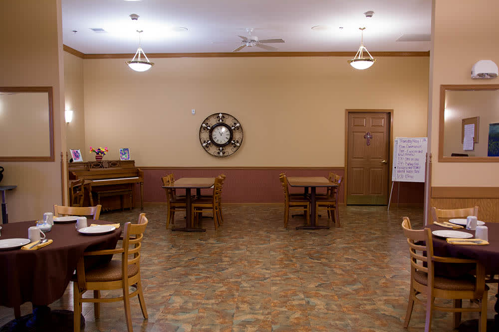 An empty dining room with wooden tables and chairs, adorned with a large wall clock.