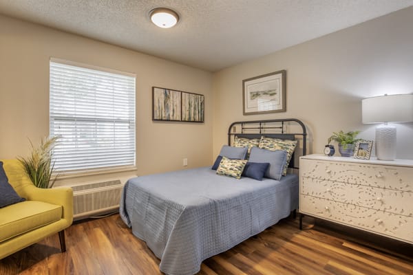 A cozy bedroom with a neatly made bed, artwork on the walls, and hardwood flooring.