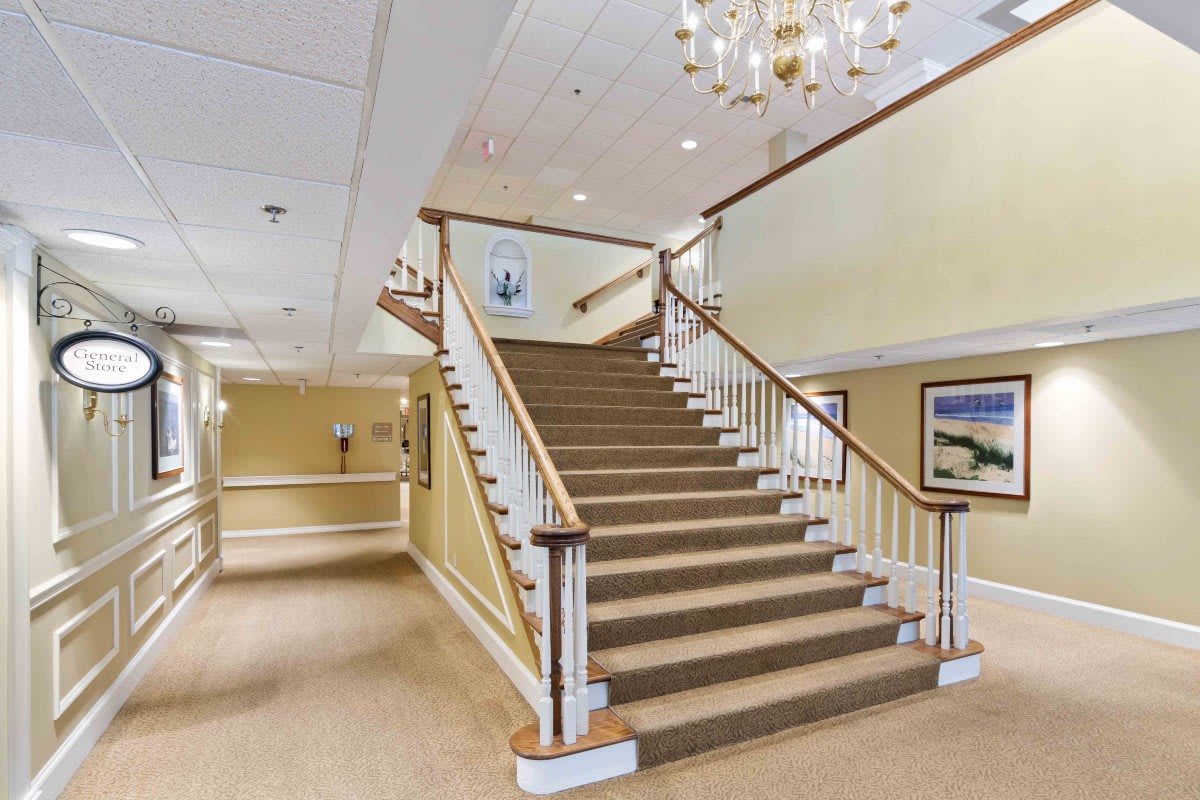 A spacious lobby featuring a grand staircase with railings, adorned by a chandelier and artwork on the walls.