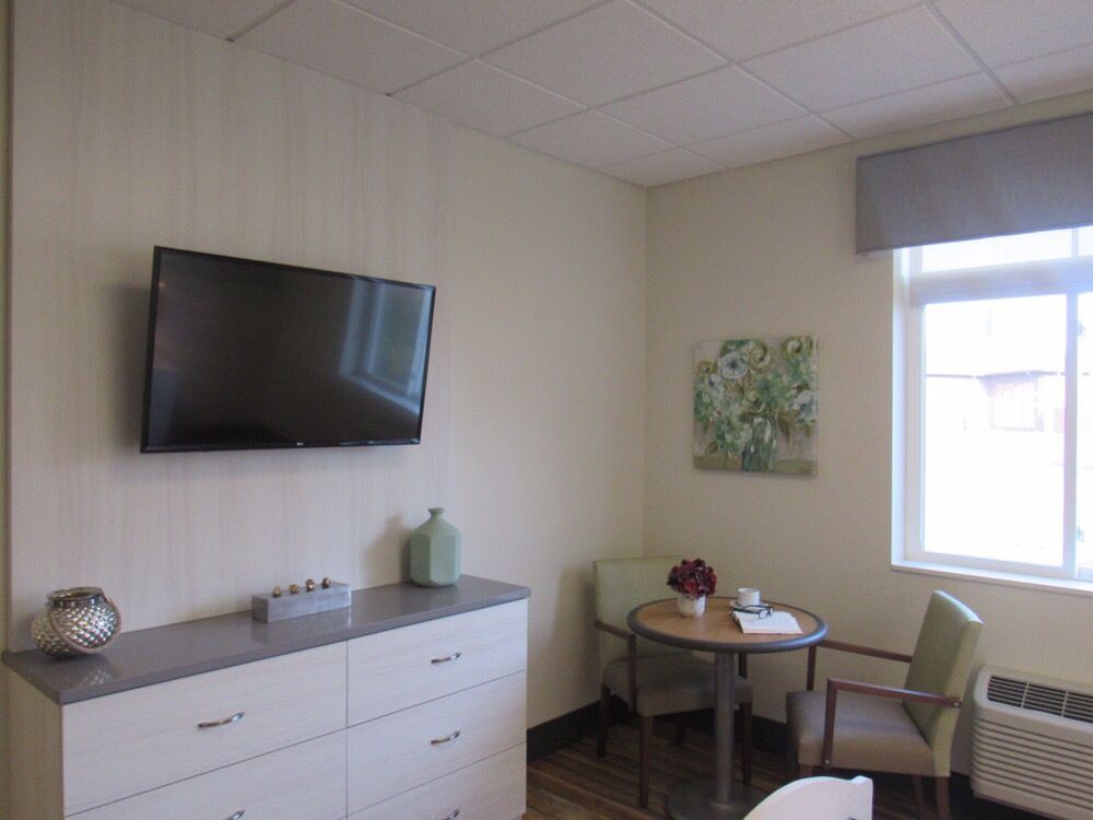 A modern room interior with a television, dresser, table, and chairs near a window.