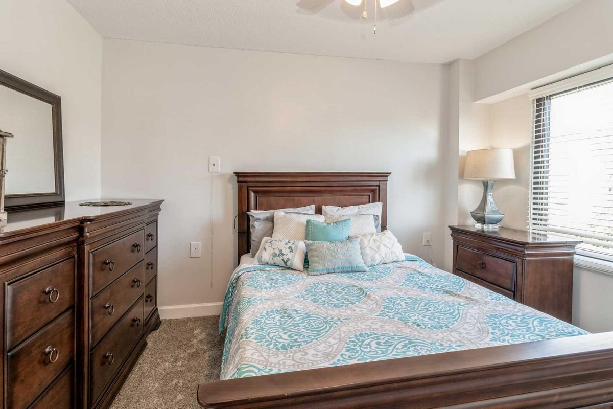 A cozy bedroom with a wooden bed frame, matching dresser and nightstand, and soft blue patterned bedding.