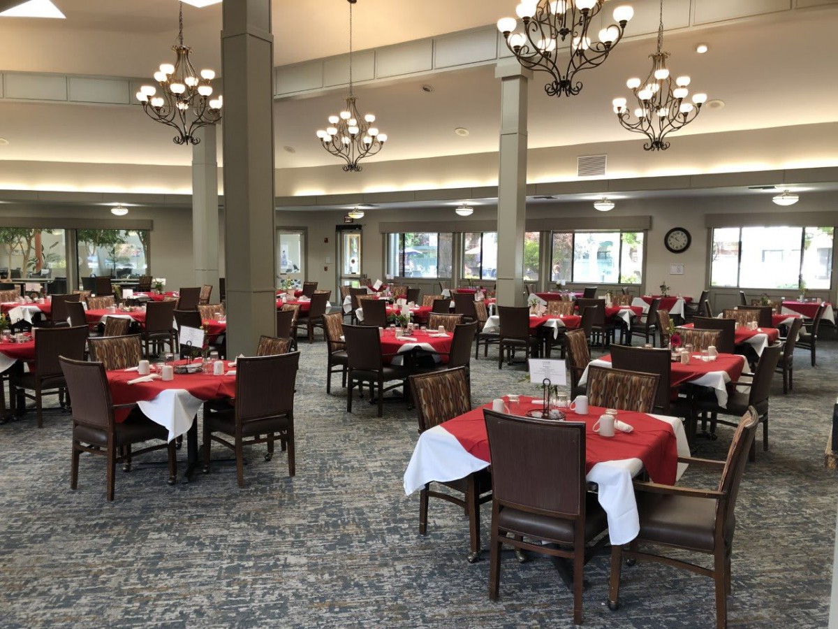 An elegant dining hall with tables set with red tablecloths and chandeliers hanging from the ceiling.