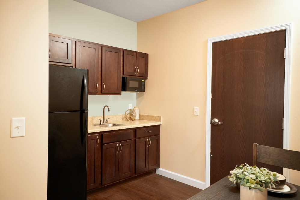 A modern kitchen with dark wooden cabinets, a black fridge, and a small countertop area.