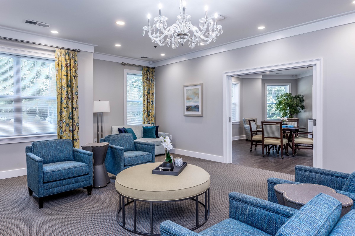 A modern and cozy living room with blue chairs, a chandelier, and a round table.