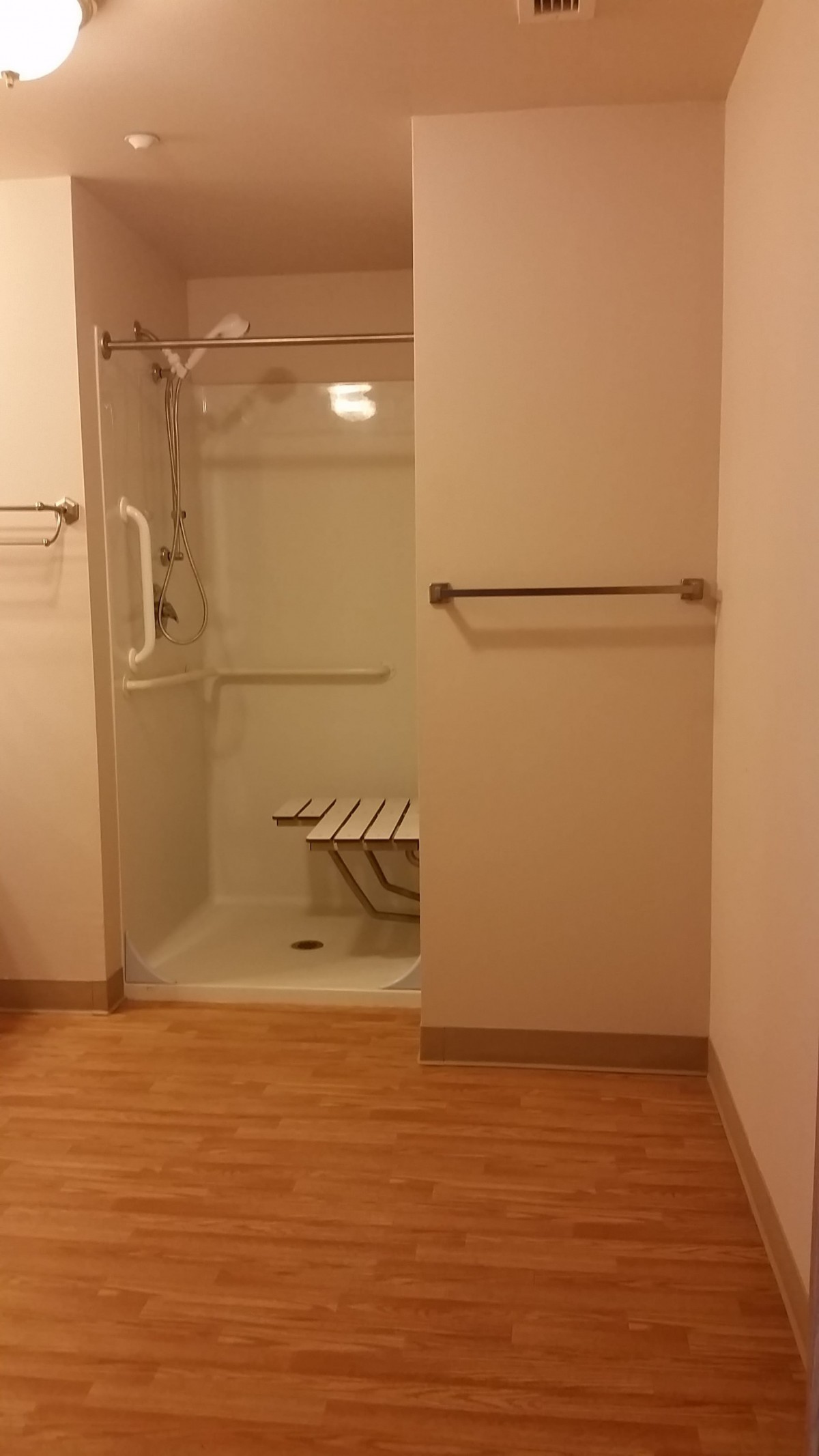 An accessible bathroom with a shower featuring grab bars and a foldable seat.