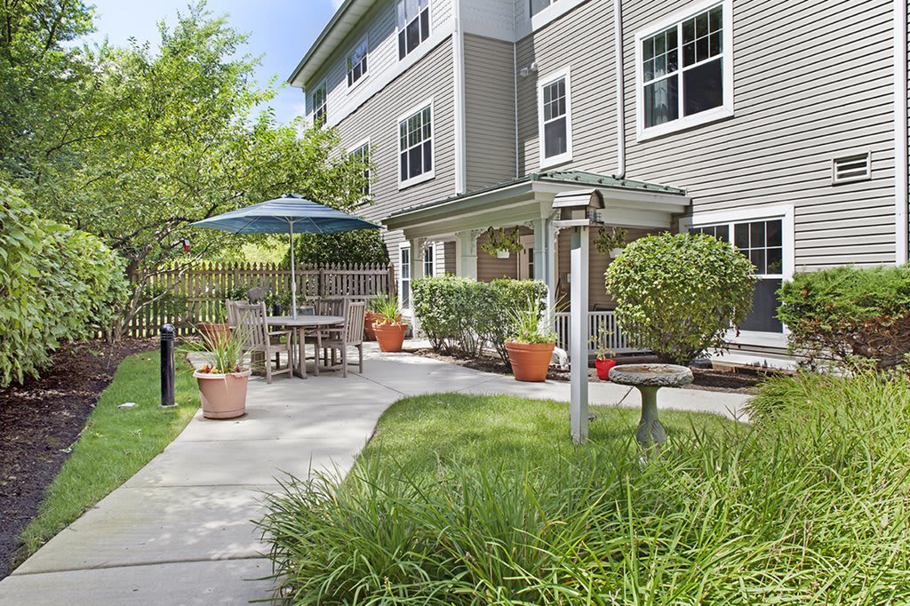 A scenic outdoor patio area with garden furniture, surrounded by greenery and a pathway.