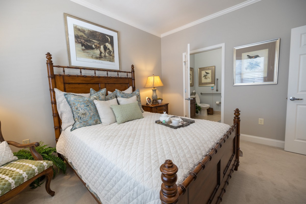 A cozy bedroom featuring a wooden bed frame, decorative pillows, and a lamp on the bedside table.