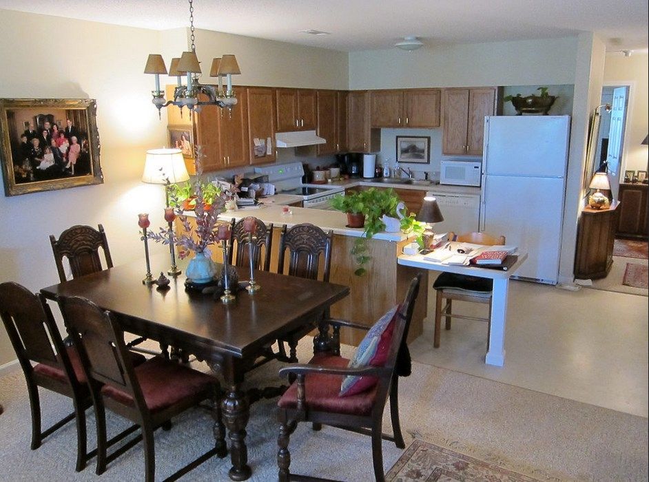 A cozy dining area connected to a kitchen, featuring a wooden table and chairs, with plants and decorative items adorning the space.