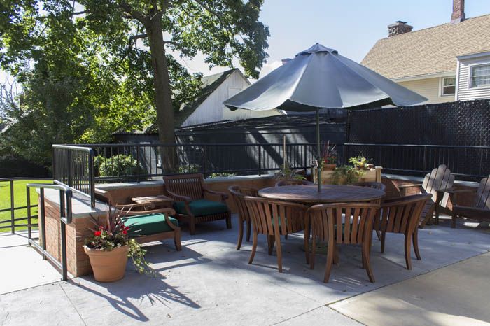 A cozy outdoor patio with wooden furniture and a large umbrella, surrounded by potted plants.