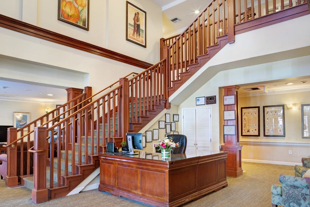 An elegant office interior featuring a wooden reception desk and staircase with artwork on the walls.