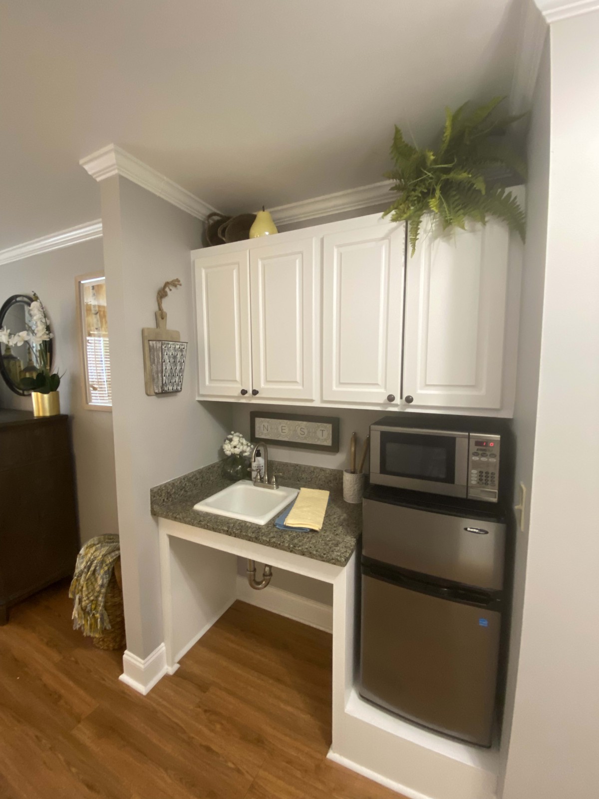 A cozy kitchen nook featuring white cabinets, a microwave, a compact fridge, and decorative plants.
