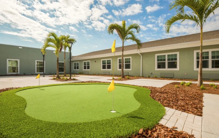 A sunny courtyard with a small putting green surrounded by palm trees and a building.
