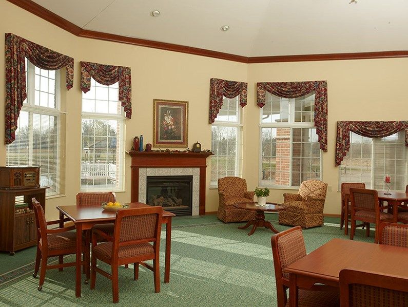 A cozy living room with tables, chairs, and a fireplace surrounded by large windows.