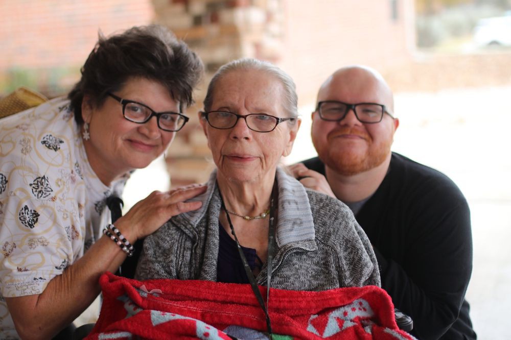 A family portrait featuring an elderly person with two smiling companions beside them.