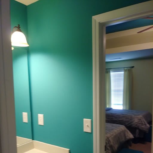 A room with teal walls and a view into an adjacent bedroom.