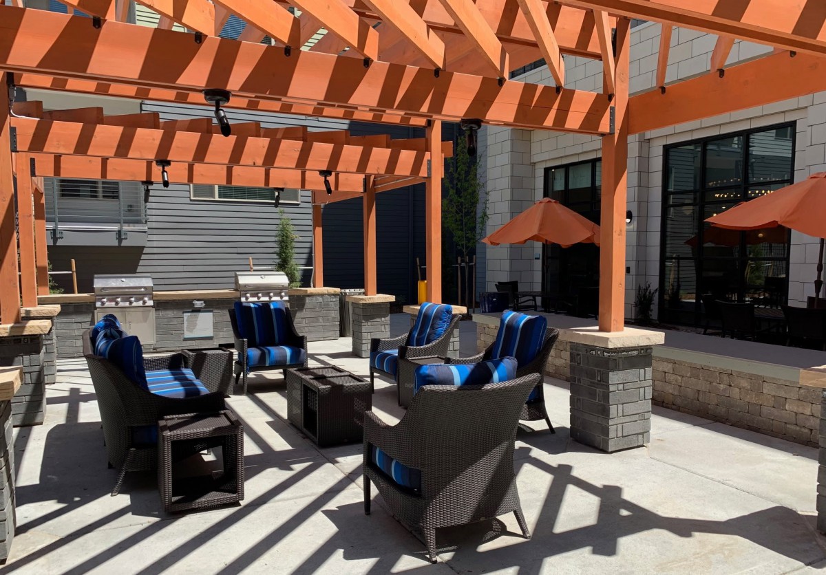 A modern outdoor patio area with a wooden pergola, featuring comfortable seating and blue-cushioned chairs.