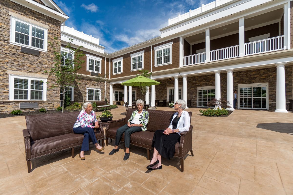Three seniors enjoying a conversation on the patio of a retirement home.