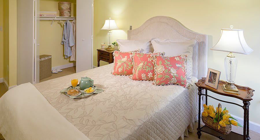 A cozy bedroom with a neatly made bed adorned with decorative pillows and a bedside lamp.