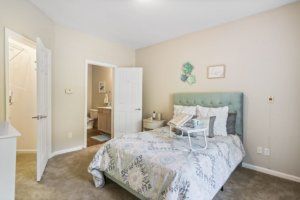 A cozy bedroom with a neatly made bed and a view into an adjoining bathroom.