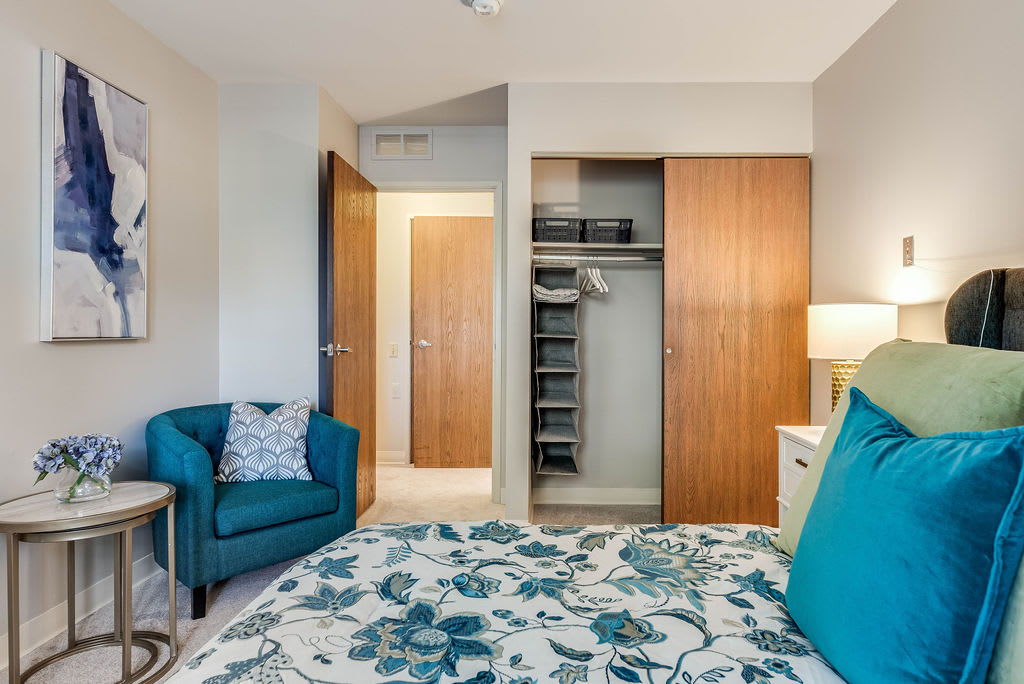 A cozy bedroom with a floral bedspread, teal armchair, and an open wardrobe.